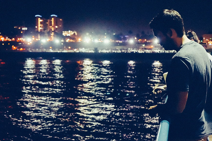 Man Fishing at Night with City Lights Reflection