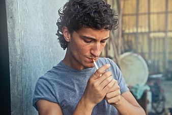 Young man lighting cigarette against concrete wall