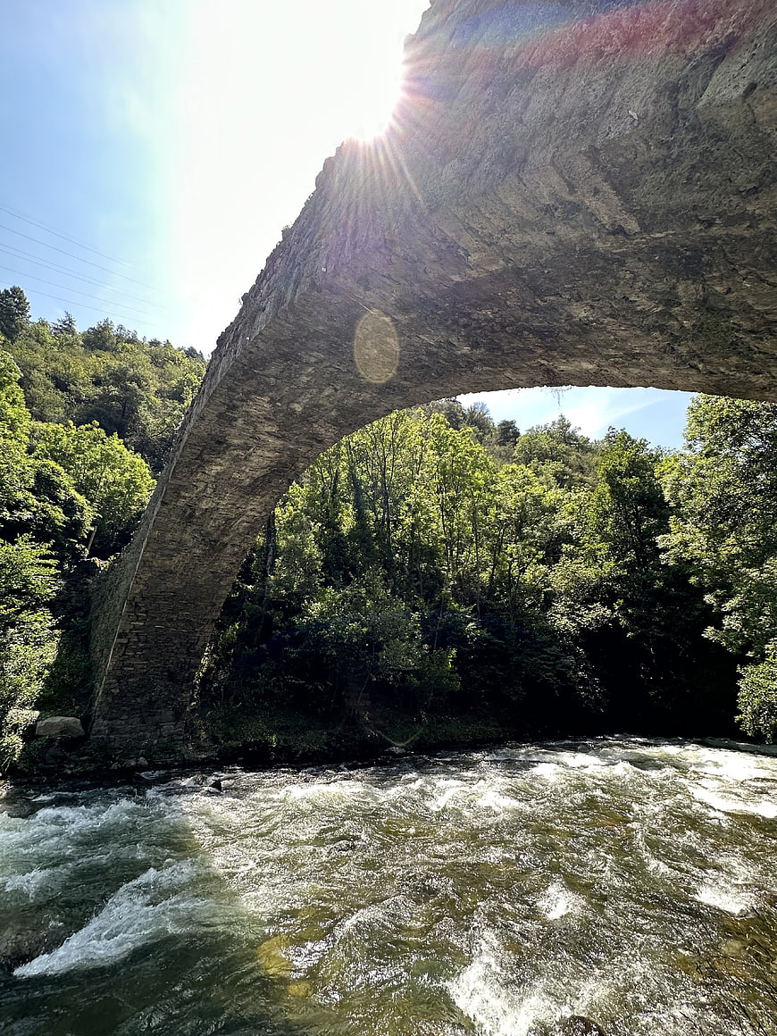 Ancient stone bridge arch over rushing river in summer forest