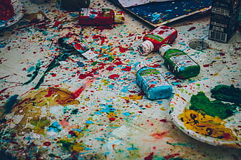 Messy artist workspace with colorful paint splatters, brushes, and bottles
