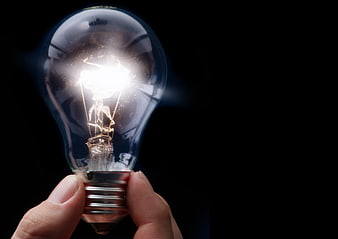 Hand holding glowing lightbulb on black background