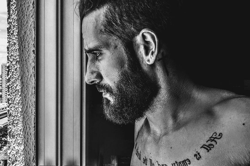 Pensive Bearded Man with Chest Tattoo Looking Out Window