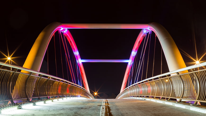 Modern illuminated arch bridge at night with colorful lights