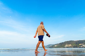 Senior man walking barefoot on beach at sunset