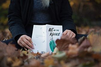Woman reading book Out of the Ruins in autumn leaves