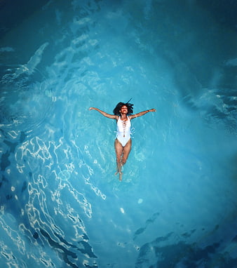 Aerial view of woman floating in blue swimming pool