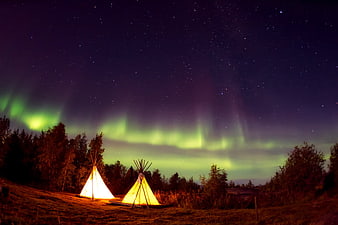 Illuminated Teepees Under Green Aurora Borealis Night Sky