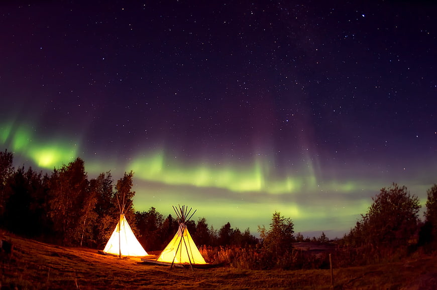 Illuminated Teepees Under Green Aurora Borealis Night Sky
