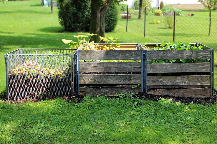 Wooden compost bins and raised garden beds in a green backyard