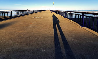 Long Shadow of Person Walking on Coastal Pier