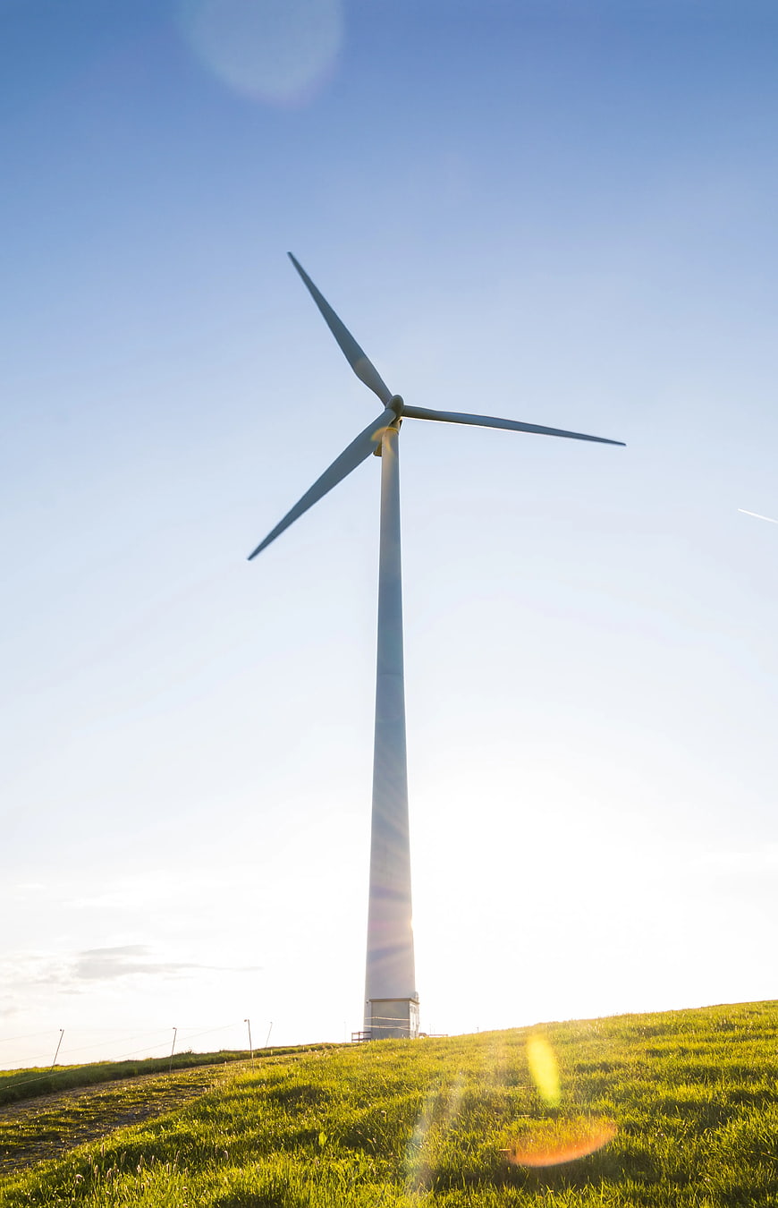 White Wind Turbine on Green Hill Against Blue Sky