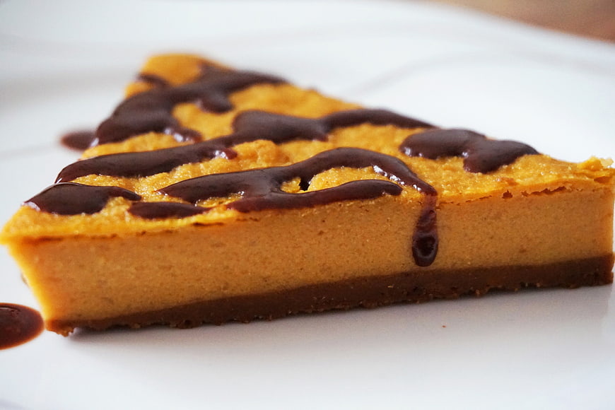 Slice of pumpkin cheesecake with chocolate drizzle on white plate