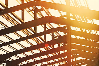 Sunlight streaming through steel beams of unfinished building roof structure