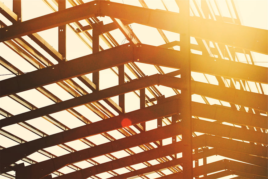 Sunlight streaming through steel beams of unfinished building roof structure