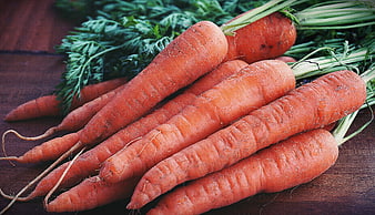 Fresh raw carrots with green tops on wooden table