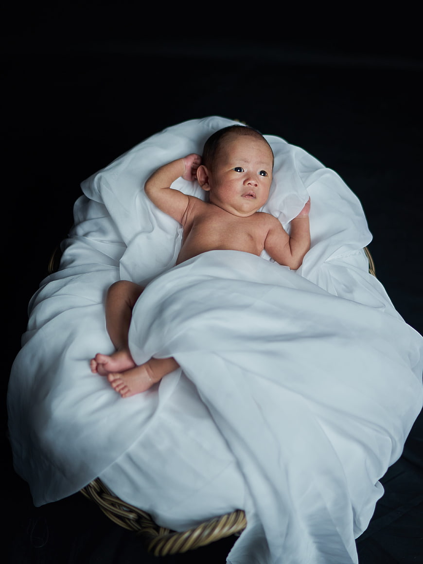 Newborn baby lying in wicker basket with white blanket
