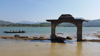 Ancient stone archway submerged in lake with boat