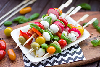 Colorful vegetable skewers with mozzarella, tomatoes, olives, and basil on a white plate