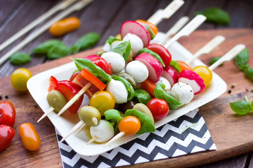 Colorful vegetable skewers with mozzarella, tomatoes, olives, and basil on a white plate