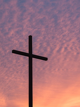 Silhouette of a cross against a pink and purple sunset sky
