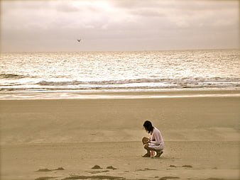 Woman Squatting on Sandy Beach with Ocean Background