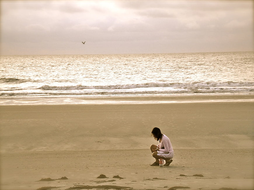 Woman Squatting on Sandy Beach with Ocean Background