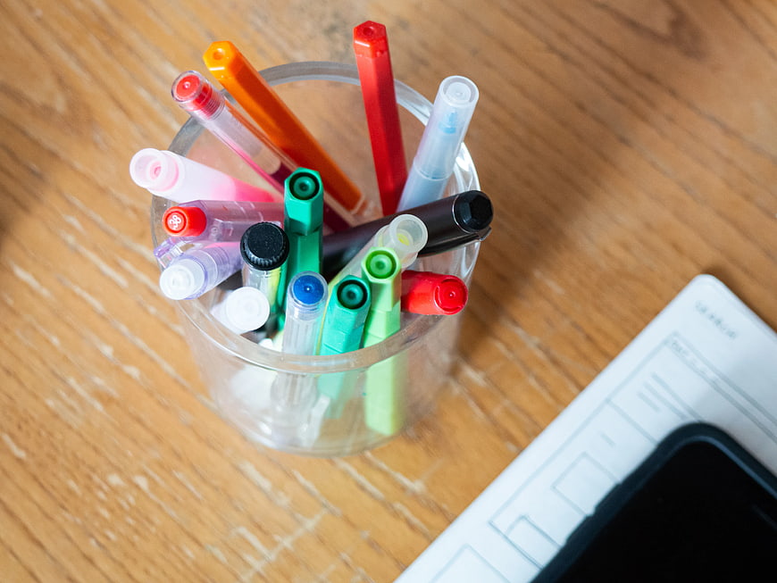 Colorful Markers in Glass Cup on Wooden Desk