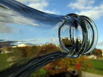 Close-up of glass bottle neck reflecting blue sky and autumn landscape