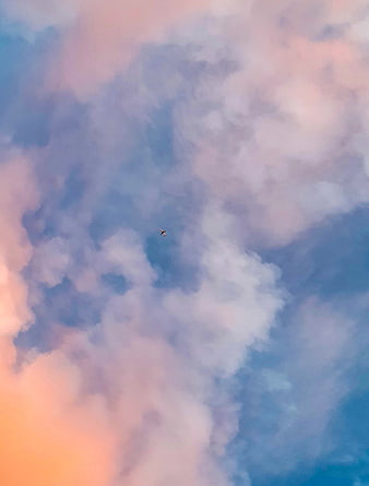 Airplane flying through pastel pink and blue clouds at sunset