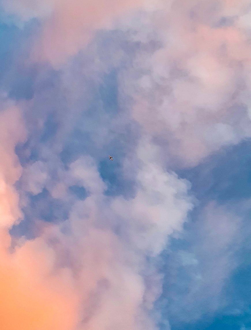 Airplane flying through pastel pink and blue clouds at sunset