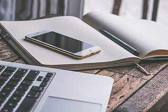 Smartphone on open notebook with laptop on rustic wooden desk