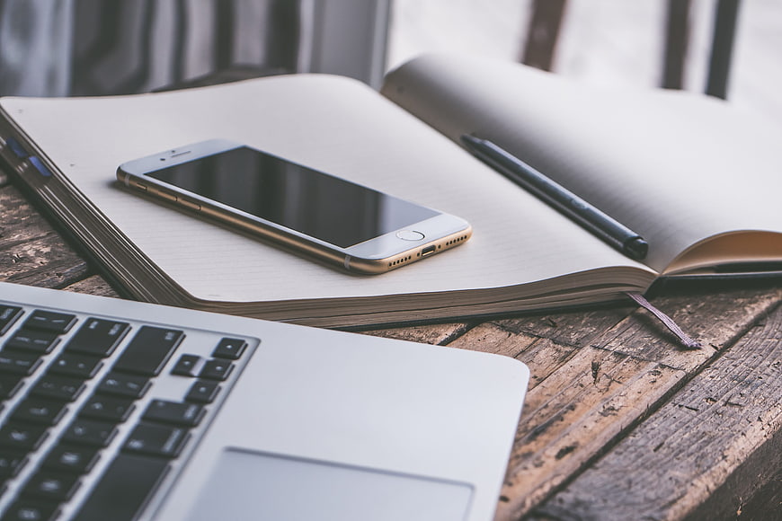 Smartphone on open notebook with laptop on rustic wooden desk