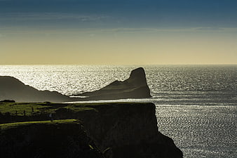 Dramatic coastal cliffs silhouetted against sparkling ocean sunset