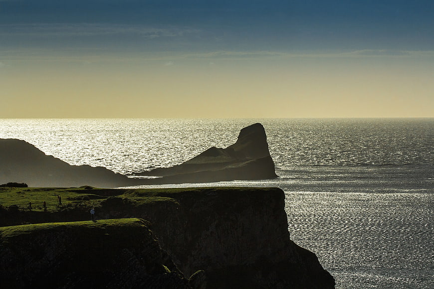 Dramatic coastal cliffs silhouetted against sparkling ocean sunset