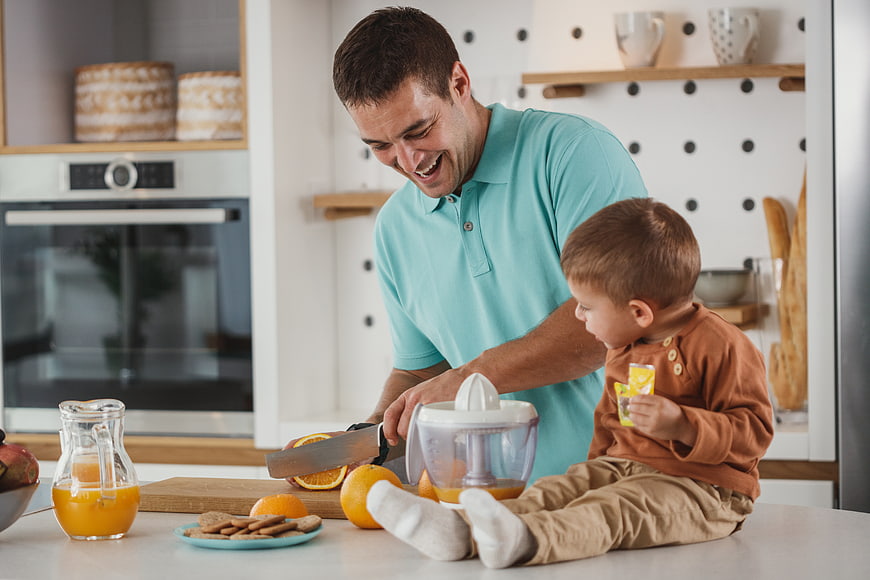 Happy father and son making fresh orange juice in kitchen