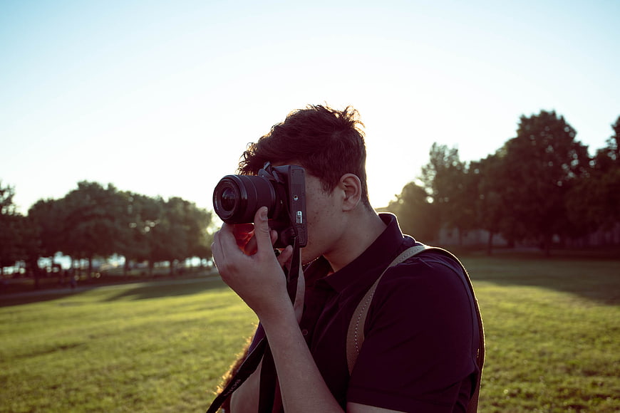 Male photographer taking photo with DSLR camera in park at sunset