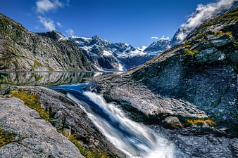 Alpine waterfall flowing into a serene mountain lake with snow-capped peaks