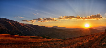 Panoramic Mountain Sunset with Golden Sun Rays and Clouds