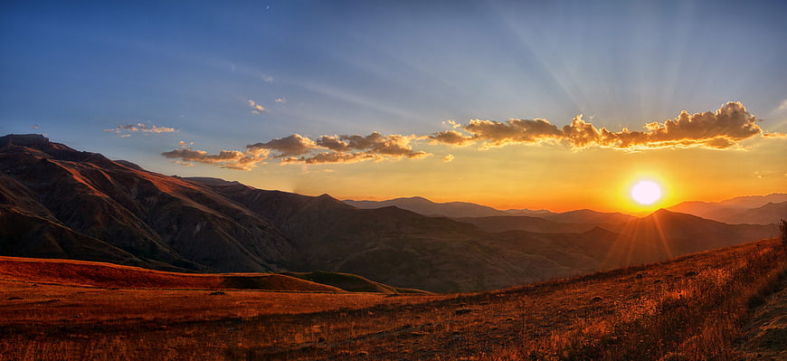 Panoramic Mountain Sunset with Golden Sun Rays and Clouds