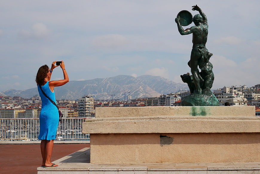 Woman photographing bronze statue with city and mountain backdrop