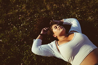 Woman relaxing in grassy field with arms behind head