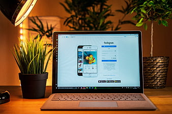 Laptop displaying Instagram app on wooden desk with potted plant