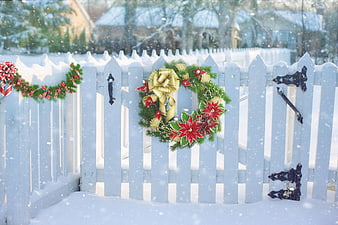 Christmas wreath on white picket fence in snowy winter