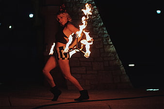 Female fire dancer performing with flaming poi at night