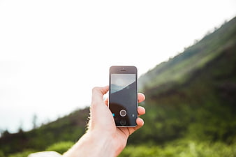 Hand holding smartphone taking photo of green mountain landscape