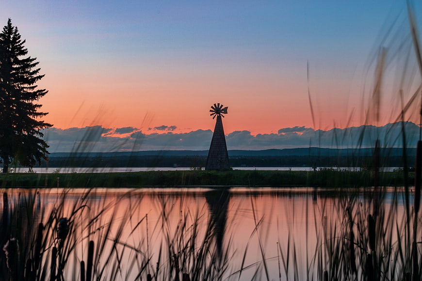 Silhouette of windmill at sunset over lake with reeds