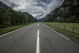 Empty Mountain Road With Dramatic Clouds And Green Pastures