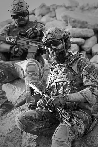 Two soldiers in tactical gear resting on rocks