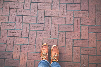First-person view of brown leather shoes on engraved brick walkway