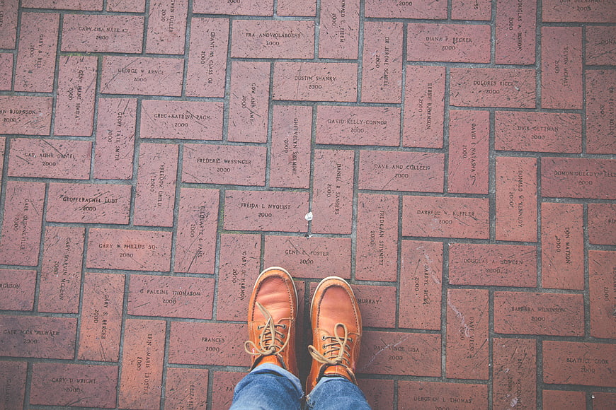 First-person view of brown leather shoes on engraved brick walkway
